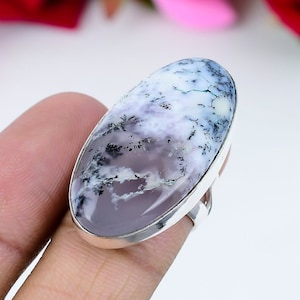 Puede incluir: Un anillo de plata con una gran piedra preciosa de ópalo dendrítico de forma ovalada. El ópalo es blanco con patrones dendríticos grises y negros.