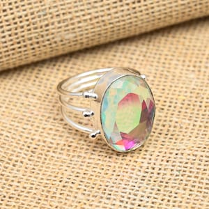 Peut inclure: Une bague en argent avec une grande pierre précieuse ovale irisée. La bague a un design à triple bande.