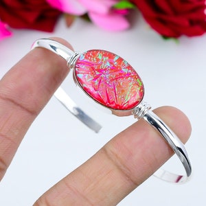 May include: A silver bangle bracelet with a pink and iridescent oval-shaped glass cabochon.