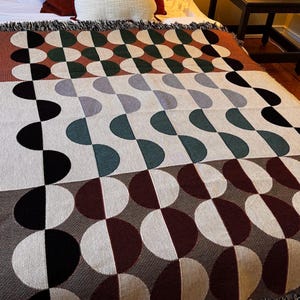 May include: A woven throw blanket with a geometric pattern of half circles in shades of brown, black, white, and green.