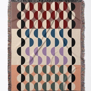 May include: A woven throw blanket with a geometric pattern of black, white, red, blue, purple, and green half circles. The blanket has a fringe border.