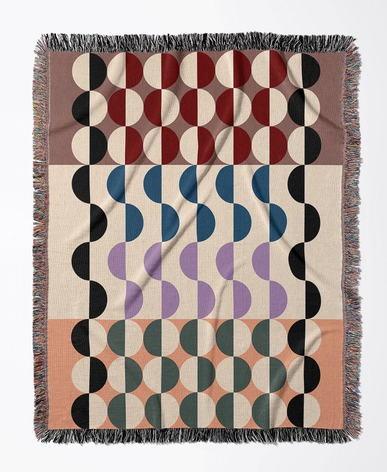 May include: A woven throw blanket with a geometric pattern of black, white, red, blue, purple, and green half circles. The blanket has a fringe border.