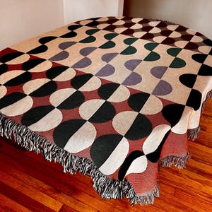 May include: A woven throw blanket with a geometric pattern of black, white, red, and green half circles. The blanket has a fringe border.