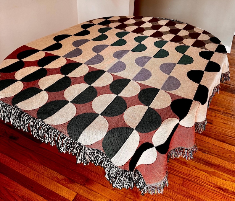 May include: A woven throw blanket with a geometric pattern of black, white, red, and green half circles. The blanket has a fringe border.