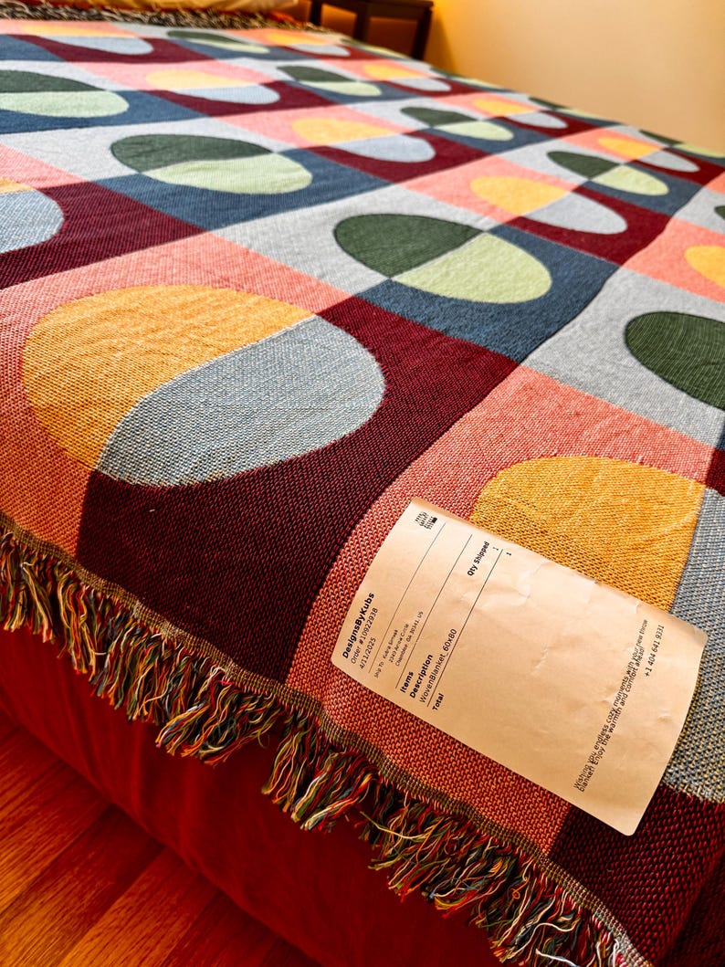 May include: A woven blanket with a colorful geometric pattern of squares and ovals in shades of red, blue, yellow, and green. The blanket has a fringed edge and measures 60x80 inches.