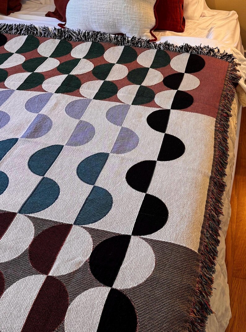 May include: A woven throw blanket with a geometric pattern of half circles in shades of red, green, blue, and black. The blanket has a fringe border.