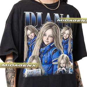 May include: Black t-shirt featuring a graphic of a young girl with long blonde hair, wearing a blue jacket. The word "DIANA" is printed above the image in a blue gradient font. The shirt has a vintage, oversized fit.