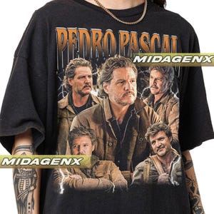 May include: Black t-shirt featuring a graphic of Pedro Pascal with the text "PEDRO PASCAL" in an orange, vintage-style font. The design includes multiple images of the actor, with lightning bolt accents. The brand name "MIDAGENX" is also visible.