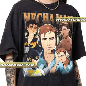 Könnte beinhalten: Dunkelgraues T-Shirt mit einem goldenen "MECHA MAN"-Grafikdesign. Das Design zeigt mehrere Illustrationen eines Mannes mit Kopfhörern und Mikrofon. Das T-Shirt hat einen Vintage-Stil.
