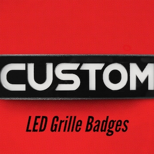 May include: Black rectangular badge with white lettering that reads "CUSTOM" and the text "LED Grille Badges" below.