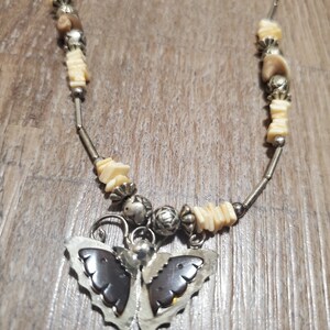 May include: A silver necklace with white and brown beads and a butterfly pendant. The butterfly has brown wings and silver accents.