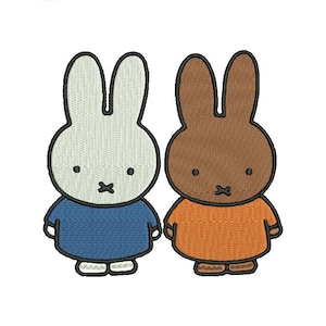 Op de afbeelding: Twee geborduurde konijnenfiguren. Eén konijn is lichtgrijs met een blauwe jurk en de andere is bruin met een oranje jurk. Beide hebben zwarte contouren, zwarte ogen en een X-vormige mond. De konijnen staan naast elkaar.