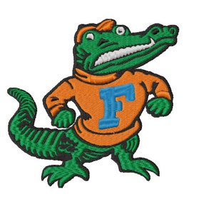 Puede incluir: Un cocodrilo verde que lleva un jersey naranja brillante con una "F" azul en la parte delantera. El cocodrilo lleva una gorra de béisbol y tiene una sonrisa de dientes.