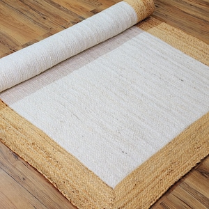 May include: A white rug with a thick, natural jute border. The rug is rolled up, showing the texture of the jute.