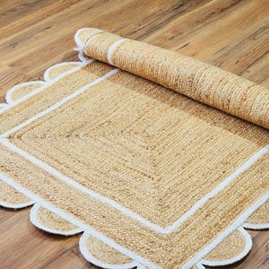 Peut inclure: Un tapis en fibres naturelles avec une bordure blanche et des bords festonnés. Le tapis est enroulé et partiellement déroulé, montrant la texture du matériau.