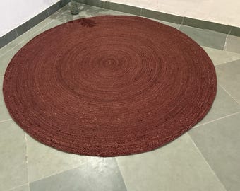 Könnte beinhalten: Ein runder, burgunderfarbener Jute-Teppich. Der Teppich besteht aus gewebten Fasern mit einem Spiralmuster, das vom Zentrum ausgeht. Der Teppich liegt auf einem hellgrauen Fliesenboden und erzeugt einen Kontrast in Farbe und Textur. Ein Einrichtungsgegenstand.