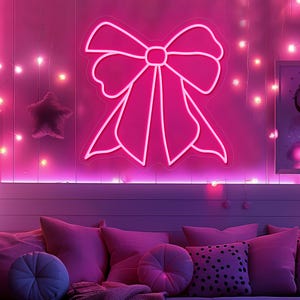 May include: A bright pink neon bow-shaped light fixture mounted on a wall. The bow is outlined in white and emits a vibrant pink glow. The wall is also illuminated with string lights and a star-shaped decoration.