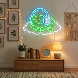 May include: A neon sign featuring a green frog wearing blue headphones, resting on a white cloud. The frog has its eyes closed and is positioned centrally. The sign emits a bright glow, illuminating the wall behind it with a soft light.