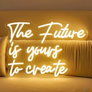 May include: A white neon sign with the words "The Future is yours to create" in a cursive font. The sign is mounted on a clear backing and emits a warm, inviting glow. The sign is placed against a yellow background.