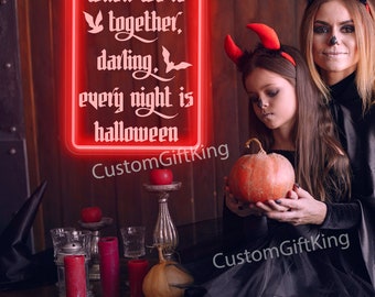 May include: Red neon sign with the text "when we're together, darling, every night is halloween". Two people dressed as devils are holding a pumpkin in front of the sign.