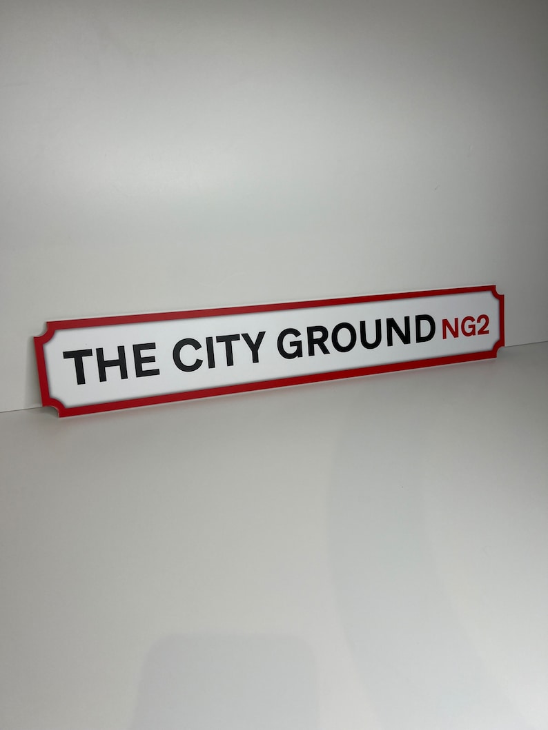 Op de afbeelding: Wit bord met rode rand en zwarte tekst die "THE CITY GROUND NG2" luidt.