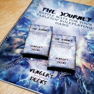 Puede incluir: Tapetes de batalla con espiral para juegos de rol de mesa. Los tapetes presentan el texto "THE JOURNEY" y "VENGER'S DECKS". Dos mazos en caja, "THE JOURNEY Quickening" y "THE JOURNEY", están encima del tapete, con un diseño de relámpagos azules y blancos.