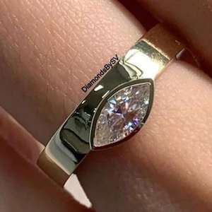 May include: A gold ring with a marquise-shaped diamond set in a prong setting. The ring is on a finger.
