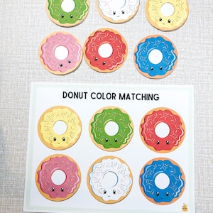 May include: Donut colour matching game with six colourful donuts with sprinkles and happy faces. The donuts are in different colours: yellow, green, red, pink, white, and blue.