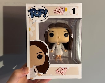 May include: A Funko Pop! vinyl figure of Lana Del Rey in a clear plastic display case. The figure is wearing a white dress and has a flower in her hair. The box features the Pop! logo and the Lana Del Rey logo.