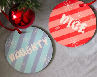 May include: Two circular ornaments with red ribbons. One ornament is light blue with diagonal stripes, white snowflake patterns, and the word NAUGHTY in white. The other is red with diagonal stripes, white snowflake patterns, and the word nice in white.