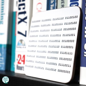 May include: White coaster with a black and white design of binary code. The code is printed in a grid pattern with rows of 0s and 1s.