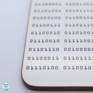 May include: A white coaster with a brown edge features a pattern of binary code, including the numbers 01100010 01101001 01110010 01111001 01101110 00100000 01100011 01101111 01110100 01100101.