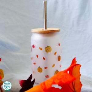 May include: A frosted glass tumbler with a bamboo lid and a metal straw. The exterior features a repeating pattern of small orange pumpkins with faces and scattered autumn leaves in shades of red, orange, and yellow. The logo Panda Motion Designs is visible.