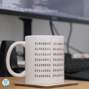 May include: White ceramic mug with black binary code printed on the side. The code reads: 01010000 01100001 01001101 01101111 01101110 00100000 01101001 01100111 011100010 0010 01101001 01111001 00100000 01100001 00100000