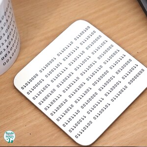 May include: A white coaster with a pattern of black binary code. The code is arranged in rows and columns, creating a visual representation of data.