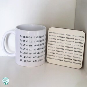 May include: White ceramic mug and coaster set with a repeating pattern of binary code. The mug has a handle and the coaster is square.