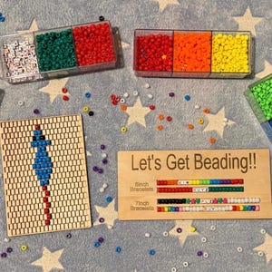 May include: A craft kit with colorful beads in clear containers, a wooden bead board with a design, and a wooden sign that says "Let's Get Beading!!" on a star-patterned surface. The kit includes beads in various colors.