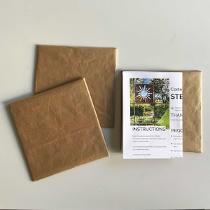 Op de afbeelding: Twee bruine papieren enveloppen en een vel papier met instructies voor een cortenstalen zonneschild. De instructies bevatten informatie over het product, veiligheidsmaatregelen en hoe het schild te hangen.