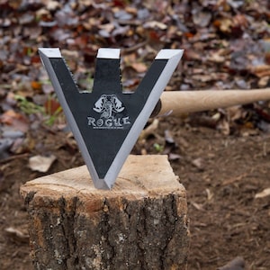 May include: A black metal tool with a triangular blade and a wooden handle. The blade has a scorpion logo and the word "ROGUE" printed on it. The tool is resting on a tree stump.
