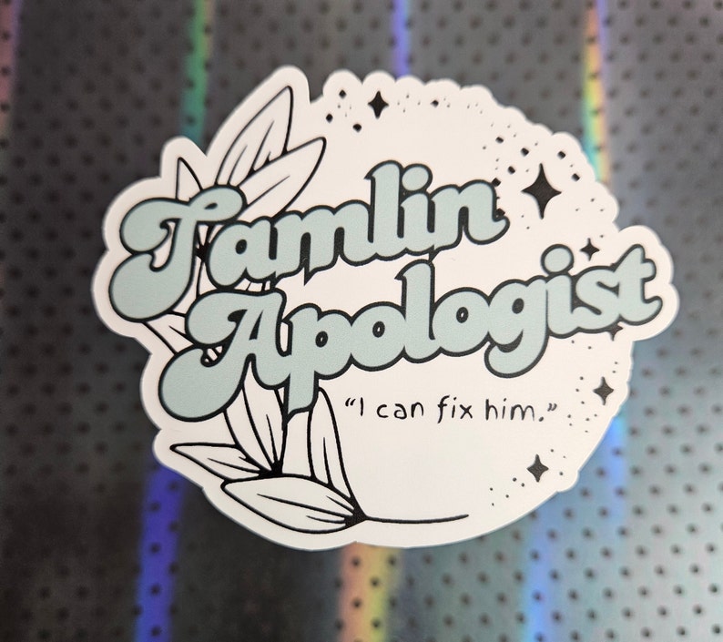 May include: A white sticker with a blue and white design. The sticker says "Famlin Apologist" in a retro font with a floral design and the text "I can fix him."