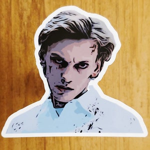 May include: A sticker of a man with short, light brown hair. He is wearing a white shirt and has a serious expression on his face. He has dark circles under his eyes and a scar on his forehead.