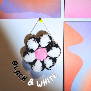 May include: A handmade, decorative flower made of black and white pom-poms with a pink center. The flower is hanging from a white string attached to a yellow push pin. The words "BLACK & WHITE" are written in a playful font.