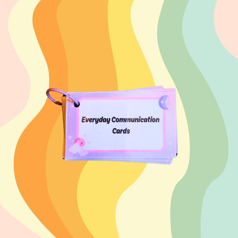 May include: A stack of Everyday Communication Cards with a purple border and a silver ring. The cards have a white background with the text "Everyday Communication Cards" in black. The background is a colorful, wavy pattern.