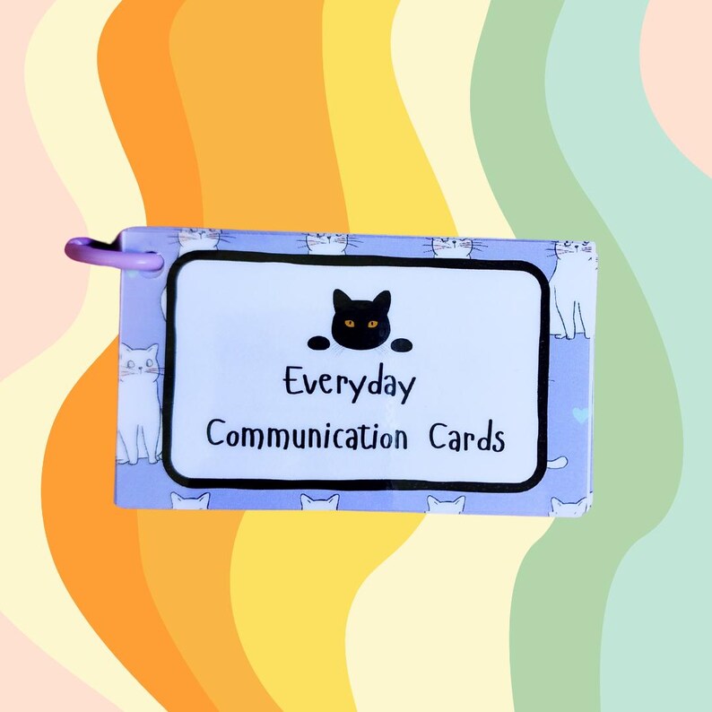 May include: A purple card deck with a black cat illustration and the text "Everyday Communication Cards". The card deck has a white border and is decorated with a pattern of white cats on a light blue background.