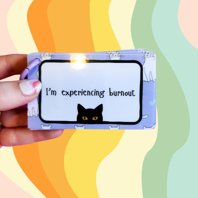 May include: A purple card with a black cat peeking over the top. The card says "I'm experiencing burnout". The card is surrounded by white cats.