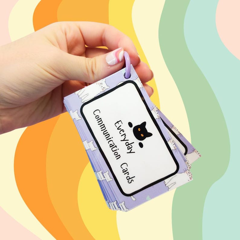 May include: A set of purple and white communication cards with a black cat logo and the text "Everyday Communication Cards". The cards are held together with a purple ring.