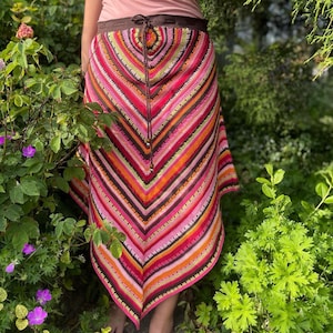 Puede incluir: Una falda de crochet colorida con una cintura marrón y un patrón geométrico. La falda está hecha con una variedad de colores, incluyendo rosa, naranja, rojo y verde.