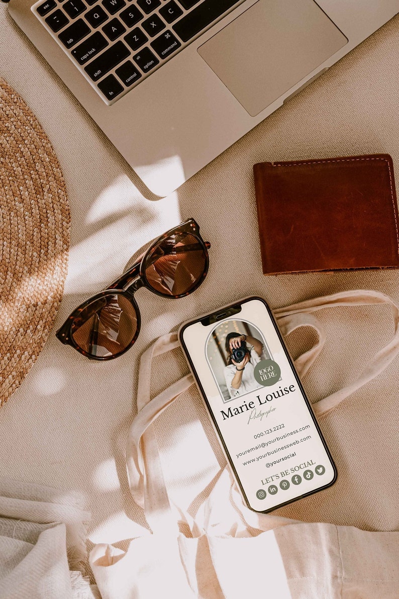 May include: A mobile phone mockup with a business card design for a photographer. The card features a photo of a woman holding a camera, the text "Marie Louise Photography", contact information, and social media icons. The phone is lying on a beige surface with a straw hat, sunglasses, and a brown leather wallet.
