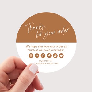 Puede incluir: Una pegatina redonda con fondo marrón y texto blanco que dice "Gracias por tu pedido". La pegatina también incluye iconos de redes sociales para Instagram, LinkedIn, Pinterest, Facebook, TikTok y Twitter. El texto "@yoursocial" y "yourbusinessweb.com" también está incluido.