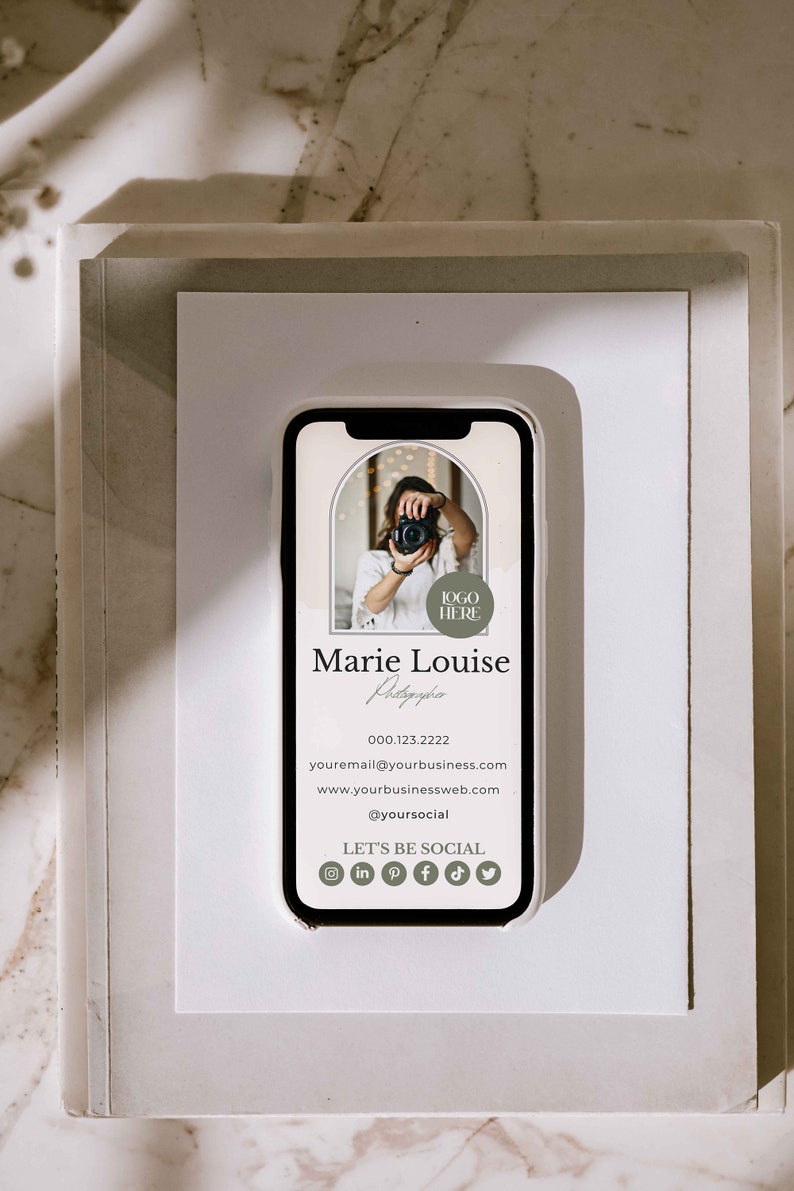 May include: A white and gray mobile phone mockup with a business card displayed on the screen. The card features a photo of a person holding a camera, the text "Marie Louise Photography", a phone number, email address, website address, social media handle, and icons for Instagram, LinkedIn, Pinterest, Facebook, TikTok, and Twitter. The text "Let's Be Social" is also displayed on the card.